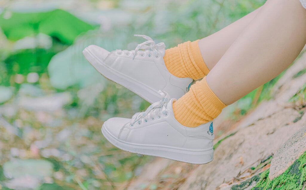 Close-up of legs in white sneakers and yellow socks outdoors, capturing youthful casual fashion.